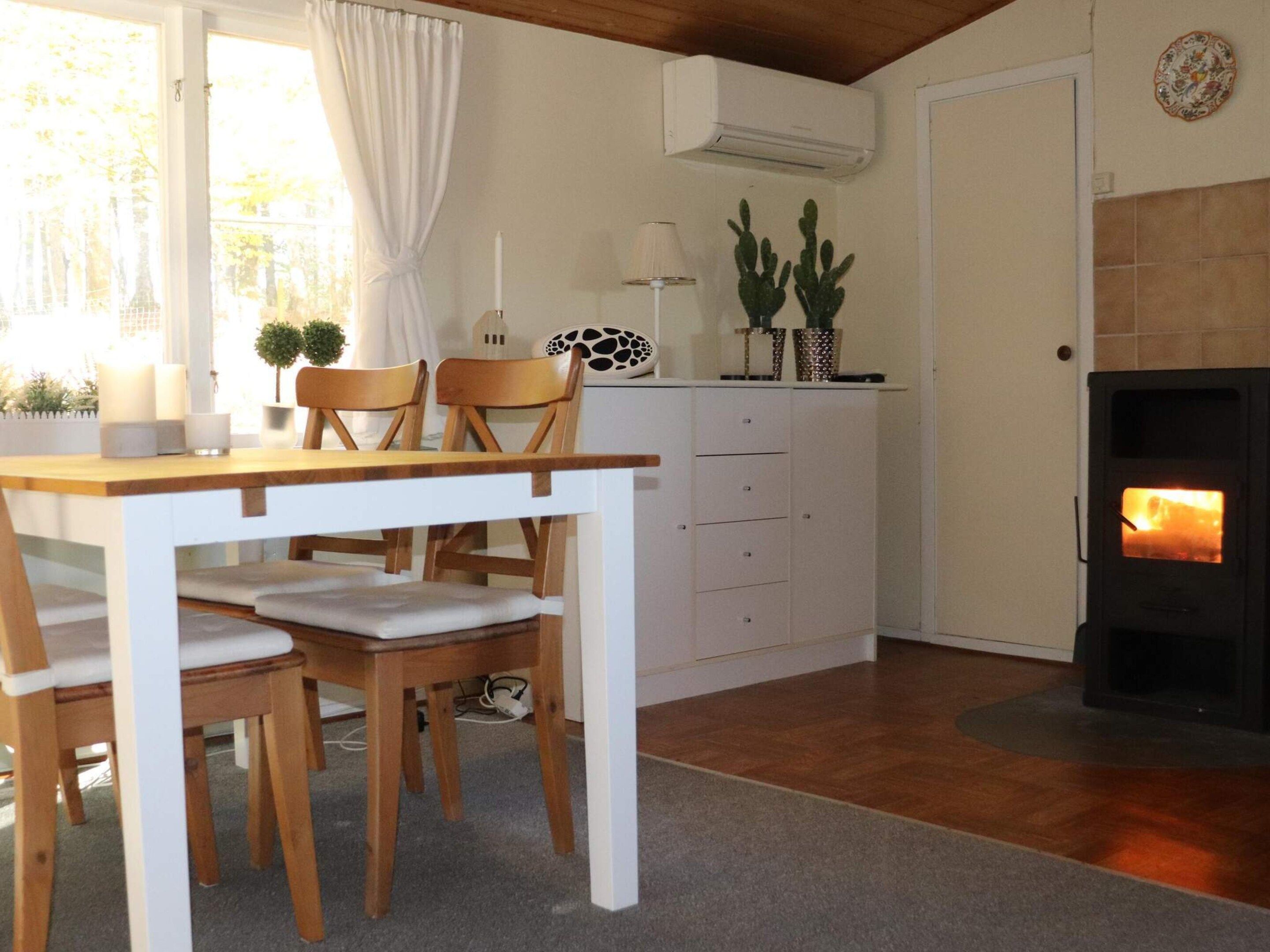 Una habitación acogedora con una mesa de madera, sillas, un armario blanco, una chimenea y una ventana con cortinas.