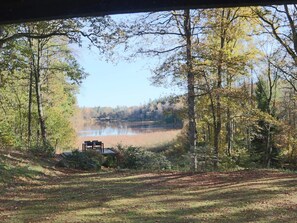 Une vue d’un lac entouré d’arbres, avec un banc et une petite construction au premier plan.