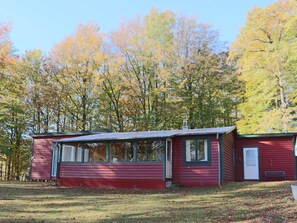 A red cabin with a small porch and a chimney, surrounded by trees with autumn foliage. - 4 Person Holiday Home in Skanes-fagerhult (Skånes Fagerhult)