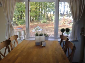 Un coin repas avec une table et des chaises en bois, une fenêtre avec des rideaux et une vue sur une zone boisée.