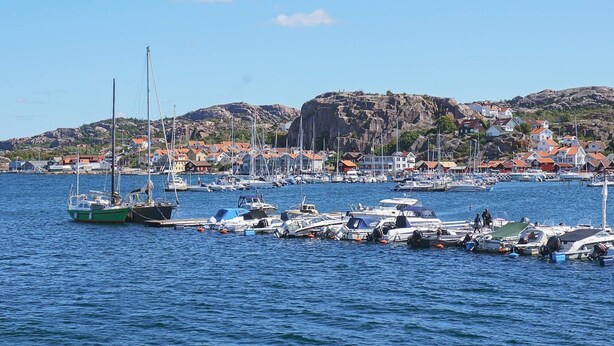 A marina with boats docked, a rocky hill in the background, and houses with red roofs. - 3 Person Holiday Home in Hunnebostrand-by Traum (Hunnebostrand)
