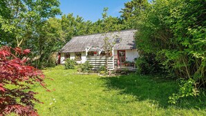 A small, traditional house with a tiled roof, surrounded by lush greenery and a well-maintained lawn. - 6 Person Holiday Home in Lokken (Lokken)
