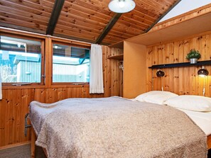 Une pièce aux murs lambrissés, avec un lit, une fenêtre et un luminaire au plafond.