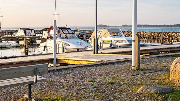 A marina with boats docked, a wooden bench, and a rocky shoreline. - 6 Person Holiday Home in Knebel (Knebel)