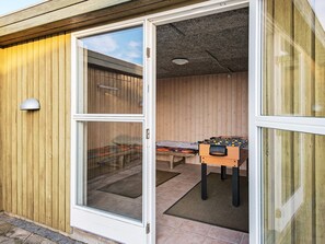 Une pièce dotée d’une porte-fenêtre coulissante donnant sur un espace extérieur, d’une table de baby-foot et d’un lit recouvert d’une couvre-lit à motifs.