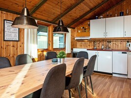 A wooden interior with a dining table, chairs, pendant lights, a kitchen area with cabinets, and a framed menu on the wall.