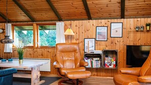 A cozy living room with wooden walls, a leather armchair, a sofa, a dining table, and a bookshelf. - 6 Person Holiday Home in Knebel (Knebel)