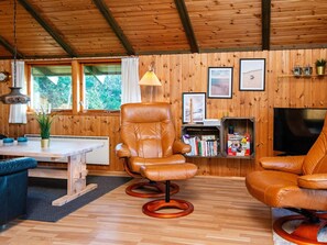 A cozy living room with wooden walls, a leather armchair, a sofa, a dining table, and a bookshelf. - 6 Person Holiday Home in Knebel (Knebel)