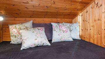 Interior de una cabaña de madera con una cama, ropa de cama floral y una lámpara de techo.