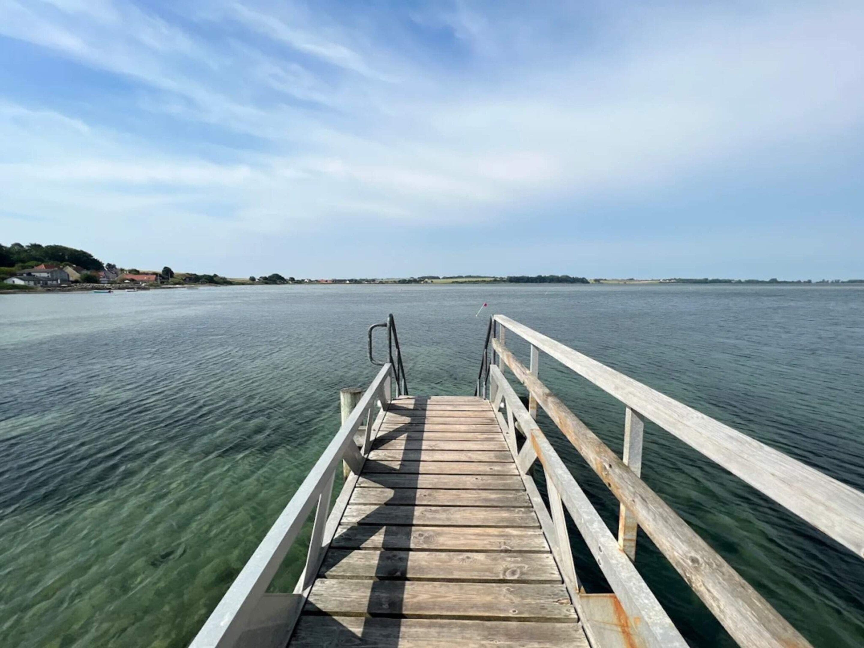 A wooden pier extending into a calm body of water with a clear sky above.