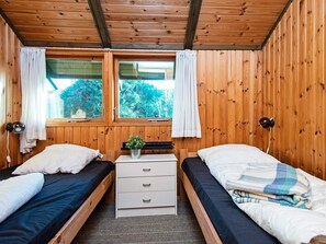 A room with two single beds, a small table with drawers, a window with curtains, and a lamp. - 6 Person Holiday Home in Knebel (Knebel)