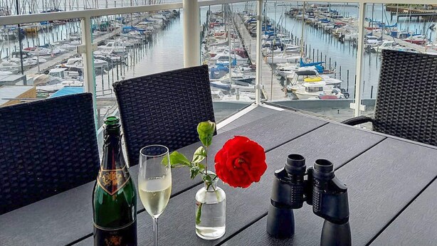 Une table avec une bouteille, un verre, un vase contenant une fleur rouge et des jumelles.