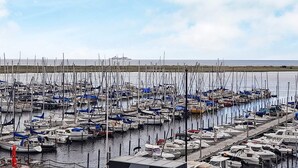 Un port de plaisance où de nombreux bateaux sont amarrés en rangées, un ciel dégagé et une mer calme en arrière-plan.