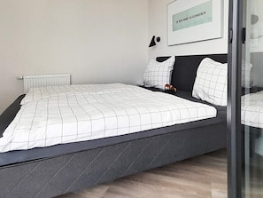 A modern bedroom with a bed, a radiator, a framed picture on the wall, and a small toy on the bed.