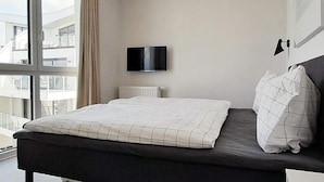 Une chambre moderne avec un lit, une télévision et une fenêtre donnant sur des immeubles.