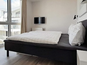 A modern bedroom with a bed, a television, and a window with a view of buildings.