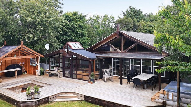 A wooden cabin with a deck, a barbecue area, and a glass-enclosed porch.