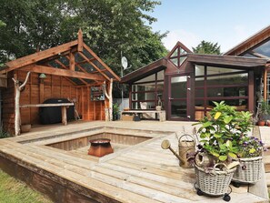 Une terrasse en bois avec un jacuzzi, des meubles d’extérieur et des plantes en pot.