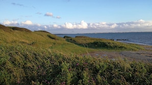 A coastal landscape with grassy hills, a body of water, and a clear sky.