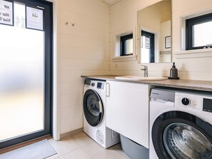 A compact laundry room with a front-loading washing machine, a sink, and a mirror above it.