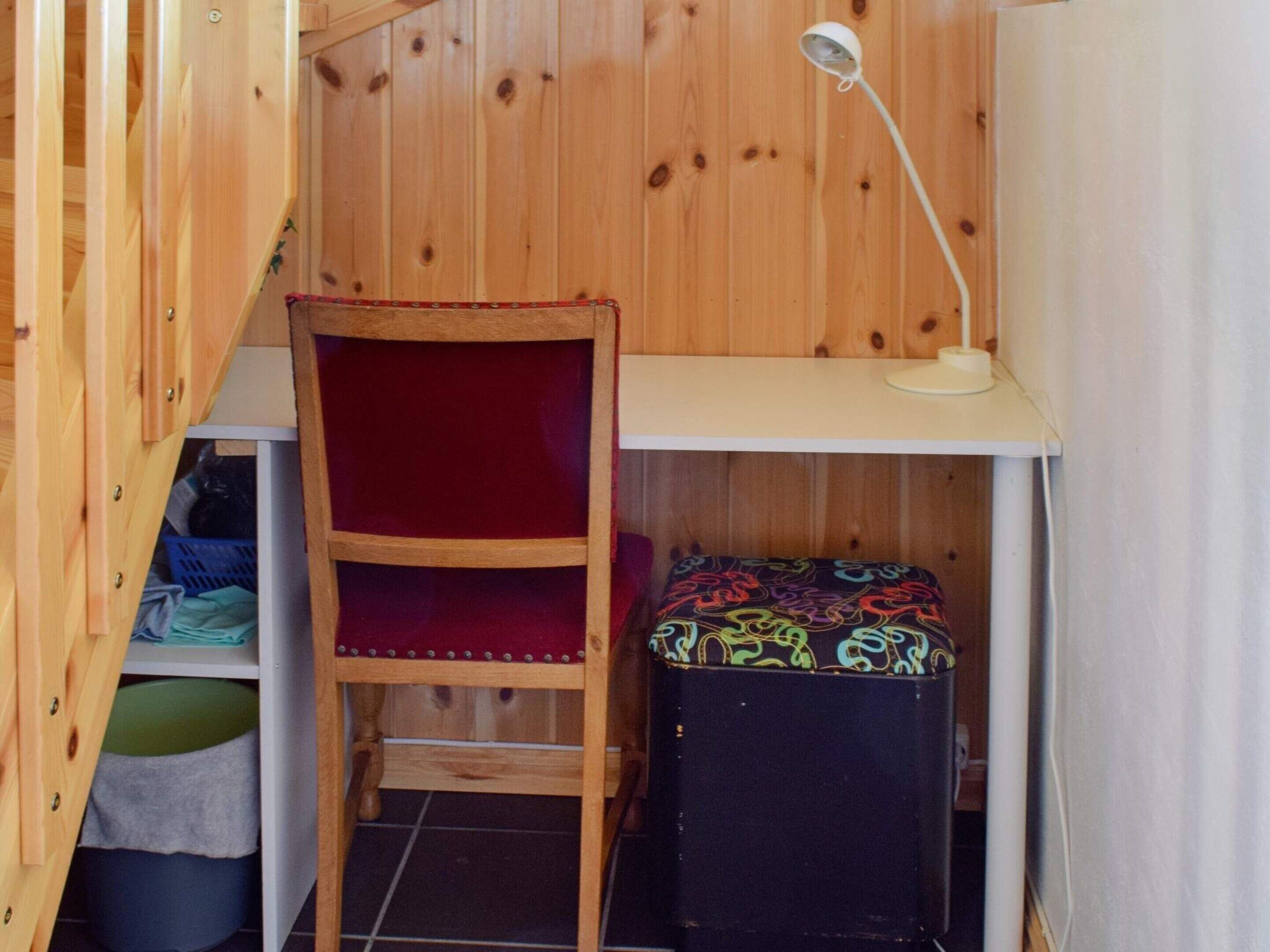 Una habitación pequeña con una silla de madera, un escritorio y un pequeño banco.