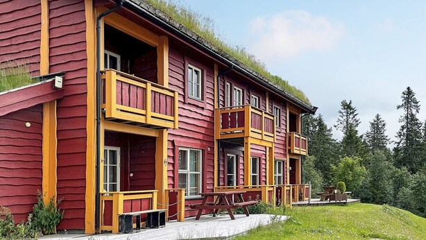 A red wooden house with yellow railings, a covered porch, and a grassy yard. - 8 Person Holiday Home in Loten-by Traum (Loten)