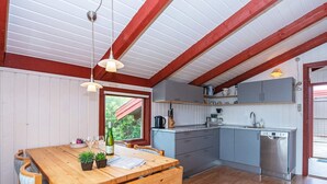 A cozy kitchen with wooden cabinets, a dining table with chairs, and a window with a view of greenery. - 6 Person Holiday Home in Hvide Sande (Hvide Sande)