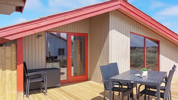 A wooden deck with a red roof, a table with chairs, and a glass door. - 6 Person Holiday Home in Hvide Sande (Hvide Sande)