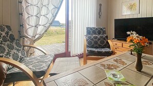A cozy living room with a wooden table, patterned chairs, a television, and a vase with flowers. - 6 Person Holiday Home in Hvide Sande (Hvide Sande)