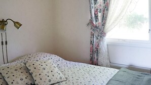 A bedroom with a bed, a bedside lamp, and a window with floral curtains. - 4 Person Holiday Home in Askloster (Åskloster)