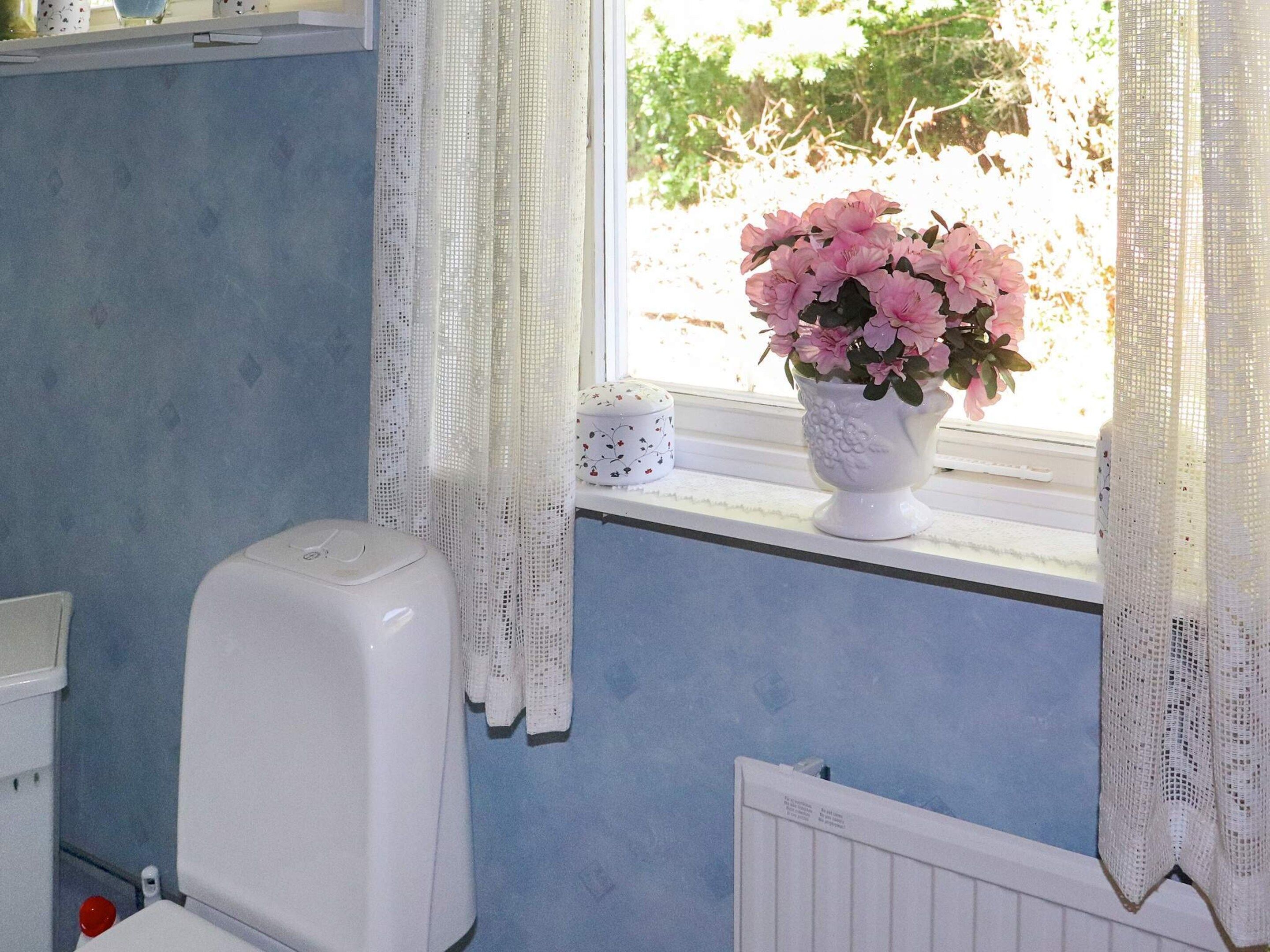 A bathroom with a toilet, a white radiator, and a window with a white curtain.