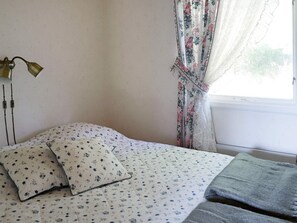 A bedroom with a bed, a bedside lamp, and a window with floral curtains. - 4 Person Holiday Home in Askloster (Åskloster)