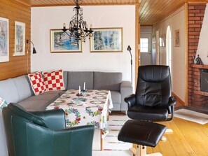 A cozy living room with a sofa, a leather armchair, a table with a floral tablecloth, a chandelier, and a fireplace. - 4 Person Holiday Home in Askloster (Åskloster)
