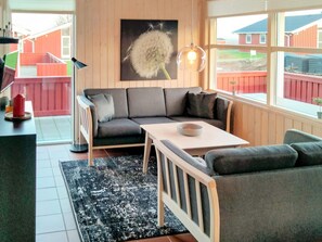 A modern living room with a sectional sofa, a dining table, and a large window with a view of a red building. - 6 Person Holiday Home in Sydals (Sydals)