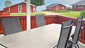 A patio with a table and chairs, surrounded by a red wooden fence, overlooking a row of red buildings. - 6 Person Holiday Home in Sydals (Sydals)