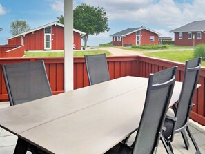 En uteplats med ett bord och stolar, omgiven av ett rött trästaket, med utsikt över en rad röda byggnader.