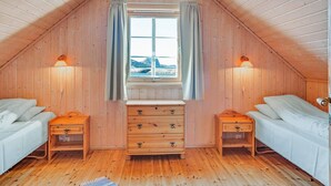 A cozy attic bedroom with wooden walls, a large window with curtains, two bedside tables with lamps, and a wooden dresser. - 6 Person Holiday Home in Brekstad-by Traum (Orland)