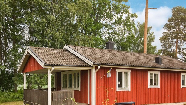 Une maison en bois rouge avec un porche, une cheminée et un petit banc.