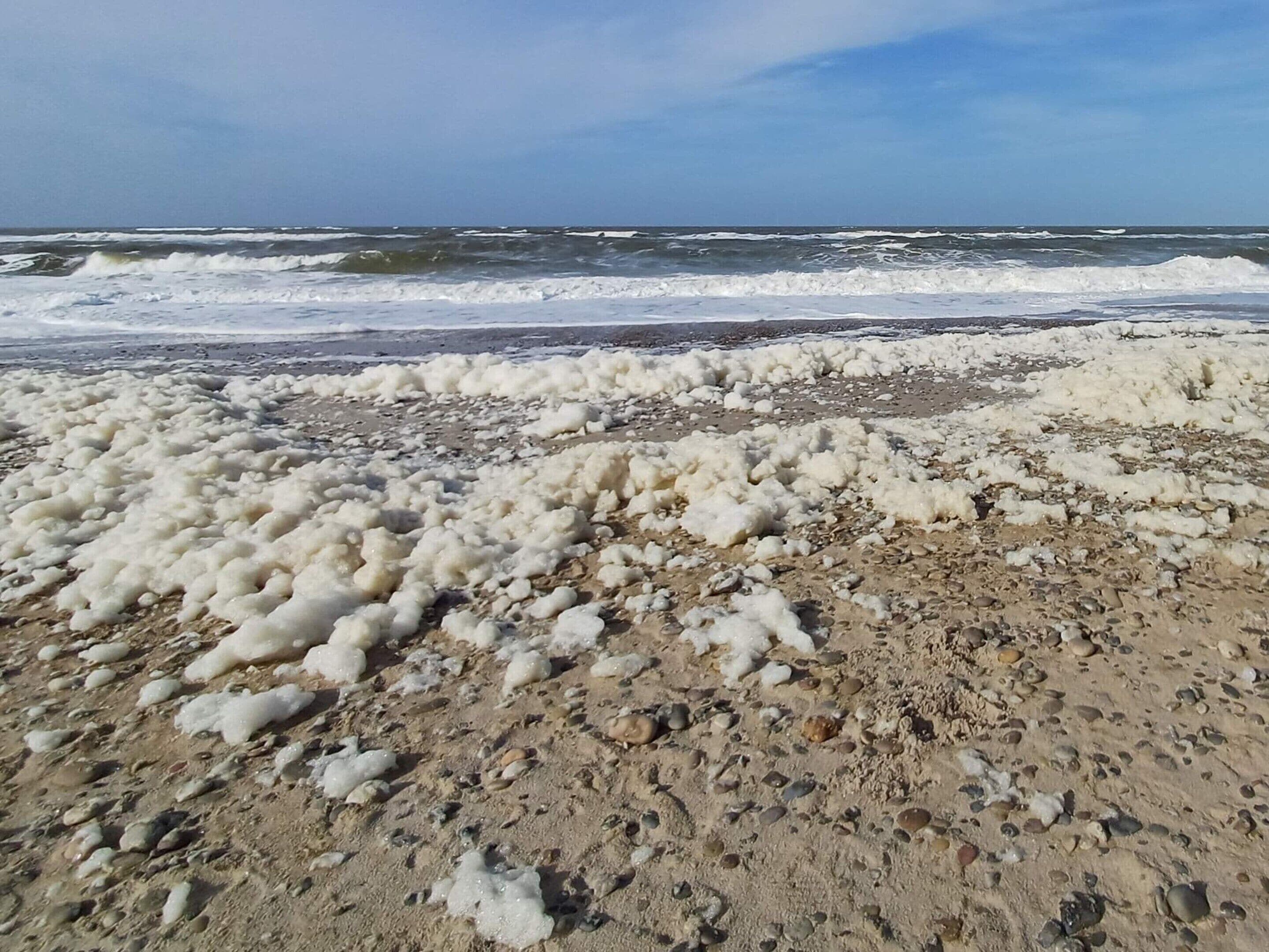 A beach with white foam on the sand and waves in the background.