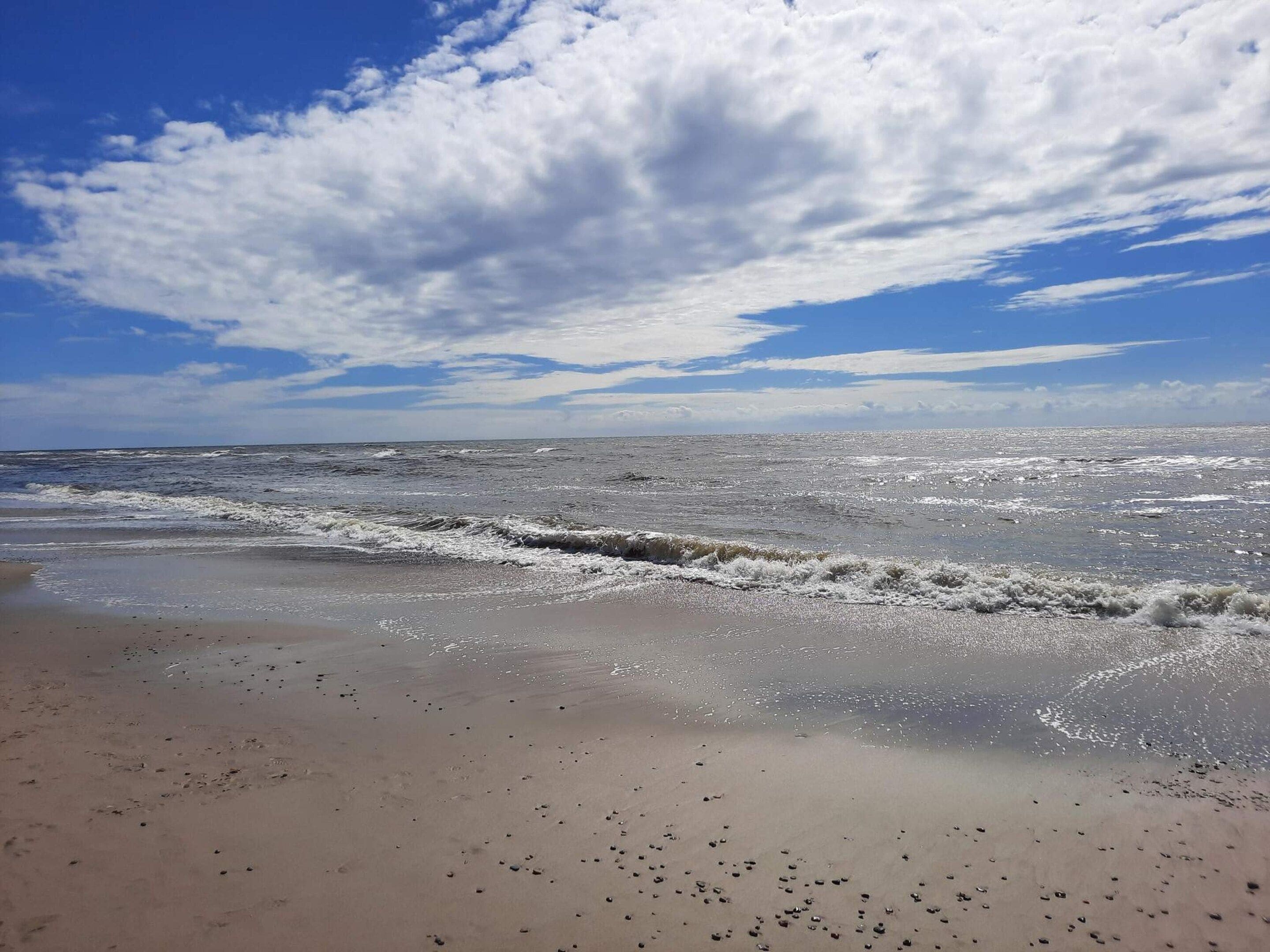 Una spiaggia con onde, cielo sereno e nuvole sparse.