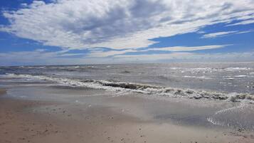 A beach with waves, a clear sky, and scattered clouds.