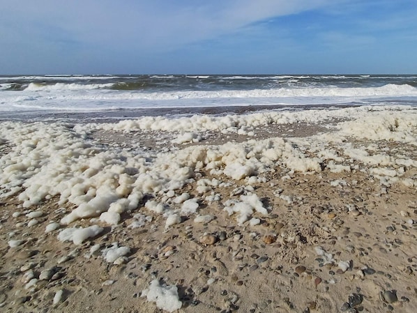 A beach with white foam on the sand and waves in the background.