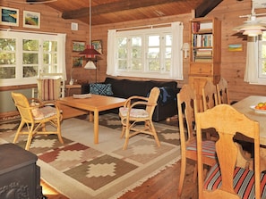 A cozy cabin interior with a wooden dining table, chairs, a sofa, and a bookshelf.