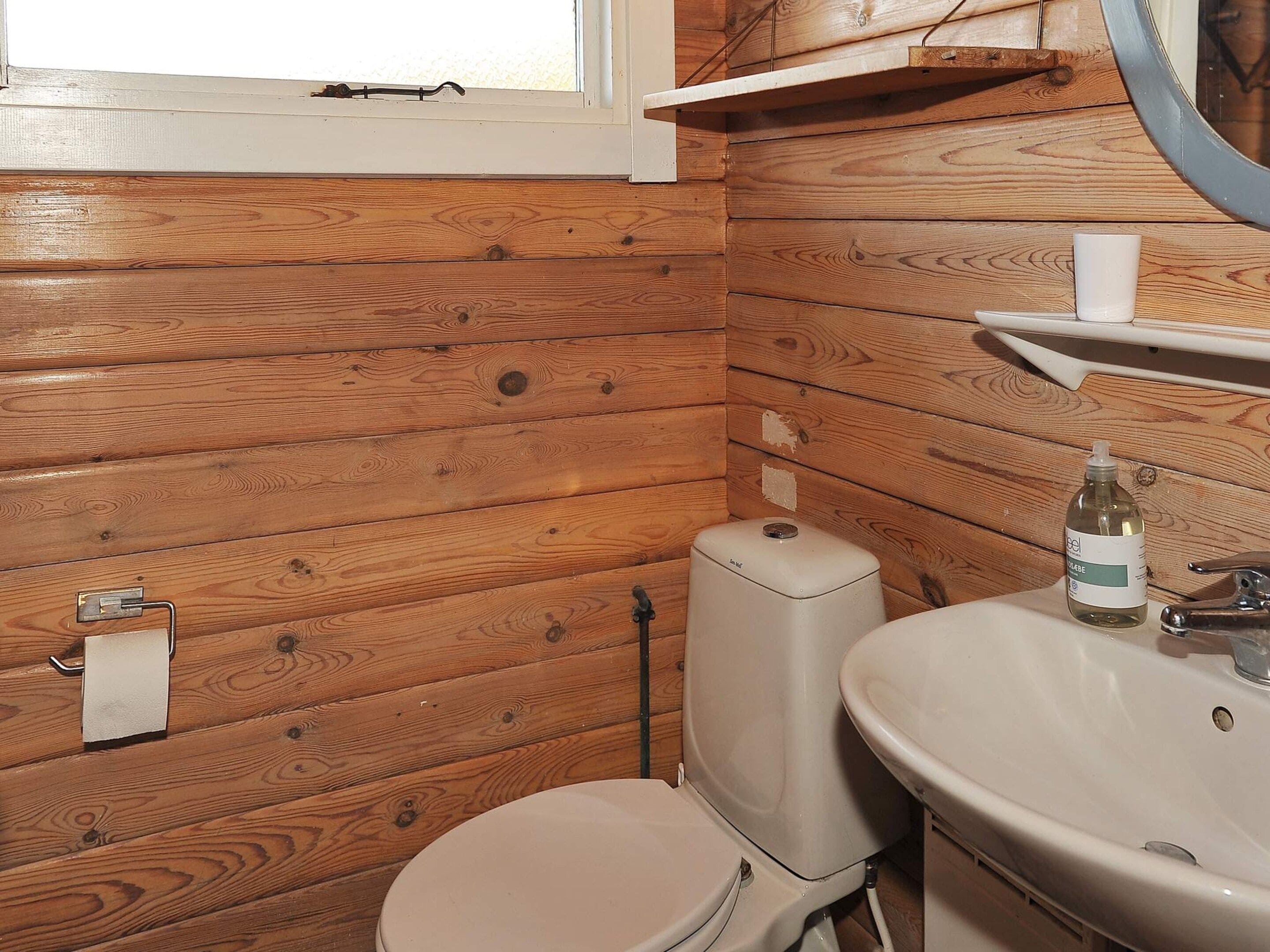 Een houten badkamer in een vakantiehuisje met toilet, wastafel en raam.