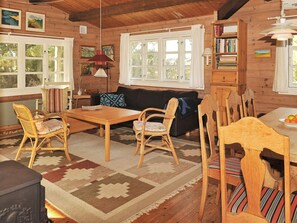 A cozy cabin interior with a wooden dining table, chairs, a sofa, and a bookshelf. - 6 Person Holiday Home in Hvide Sande (Hvide Sande)