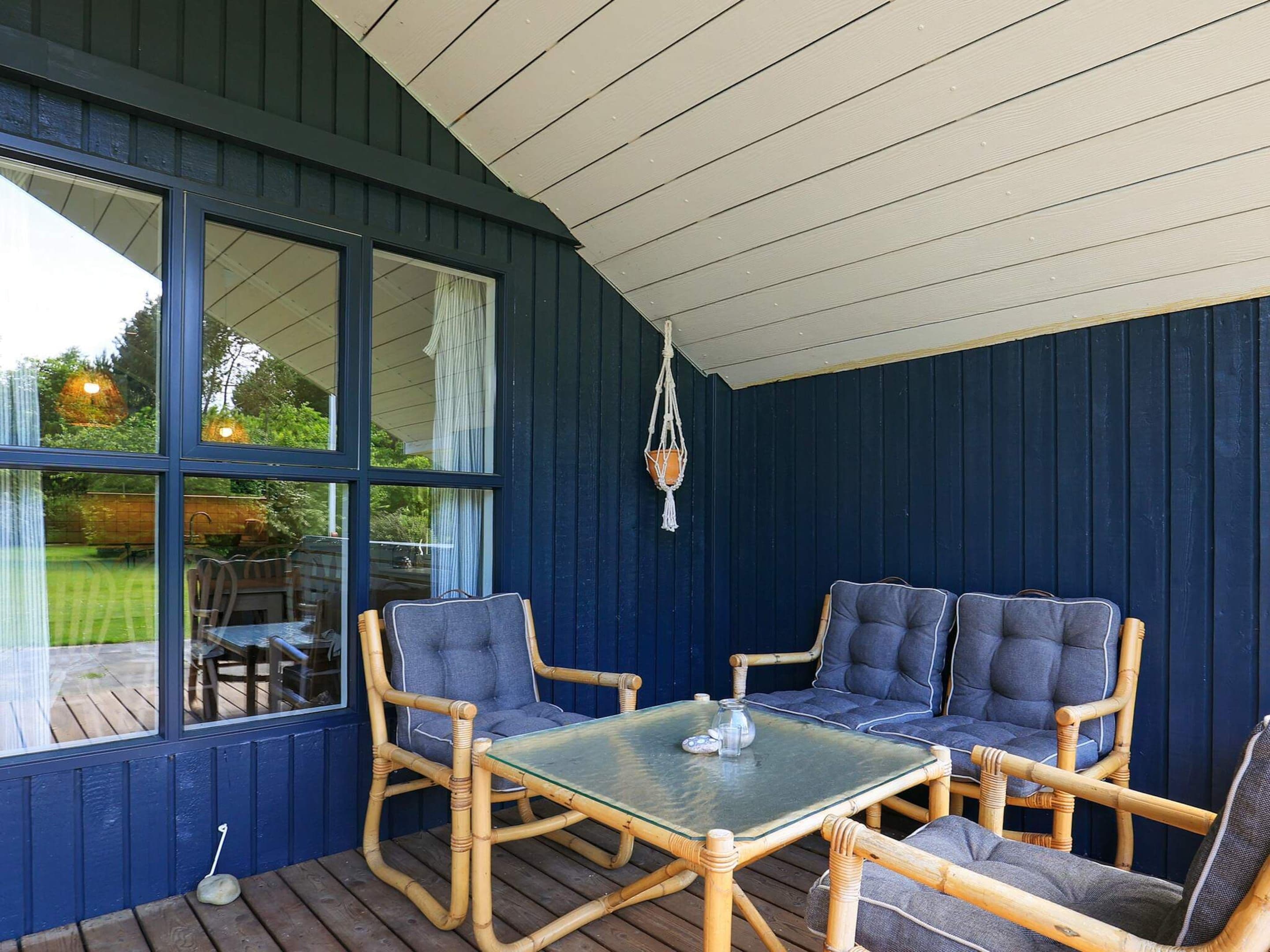 A covered outdoor seating area with a glass table, wicker chairs, and a hanging macrame light fixture.