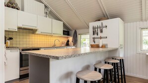 Een keuken met een centraal kookeiland, barstoelen, een magnetron en een messenrek.