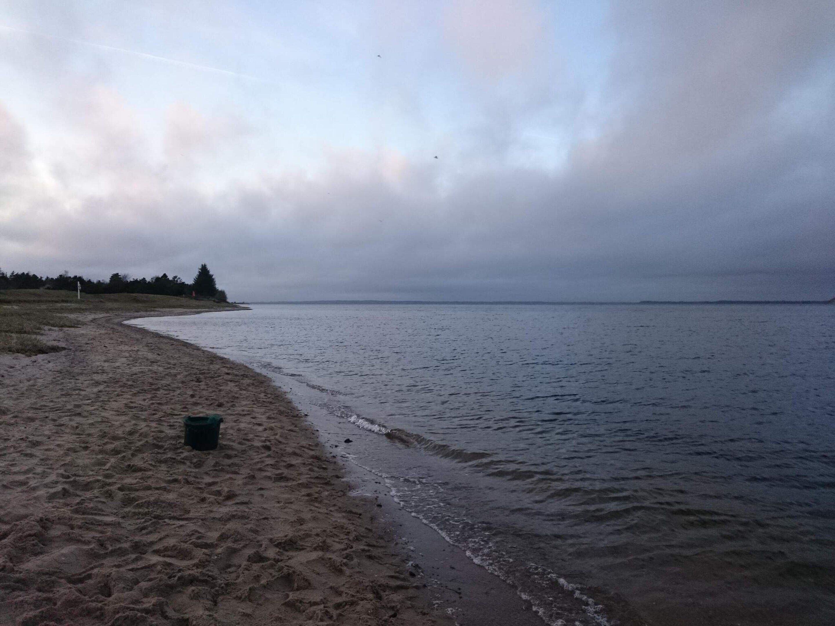 Una platja amb sorra i mar tranquil·la sota un cel nuvolós.