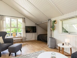 Quarto aconchegante com televisão, sofá, mesa pequena e janela com cortinas.