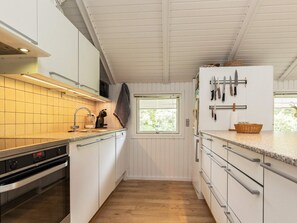 A compact kitchen with a built-in oven, a microwave, and a sink. There is a window providing natural light and a knife rack on the wall.